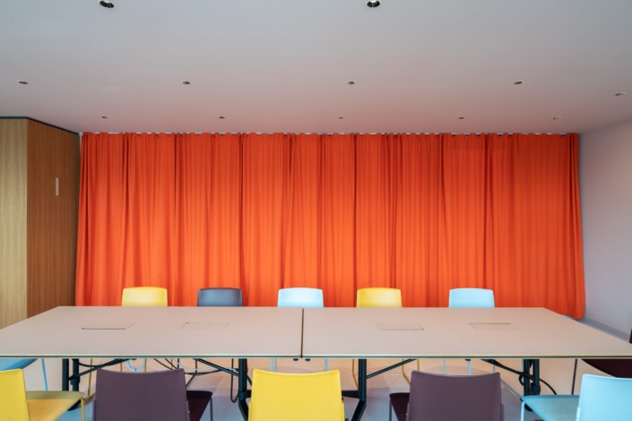 Akustikvorhang in strahlendem Orange und farbige Stühle im Konferenzraum.
